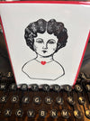 Close-up of a typewriter with a printed card featuring a stylized face and heart.