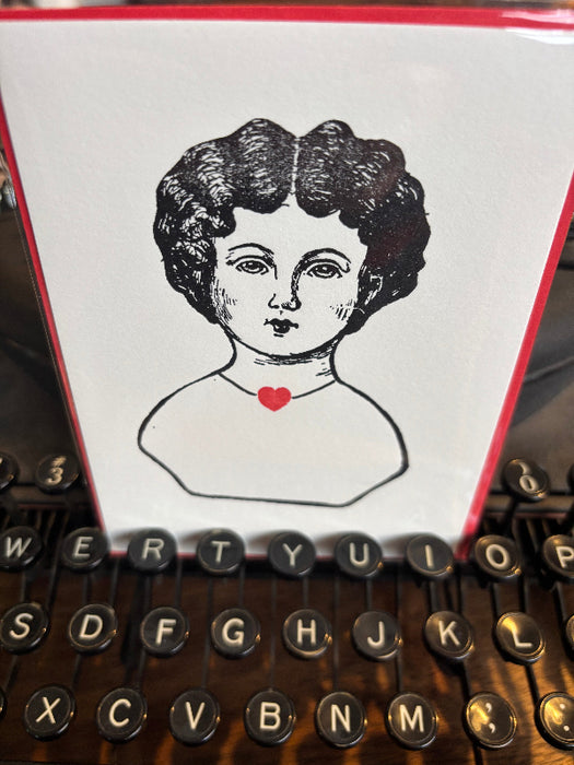 Close-up of a typewriter with a printed card featuring a stylized face and heart.